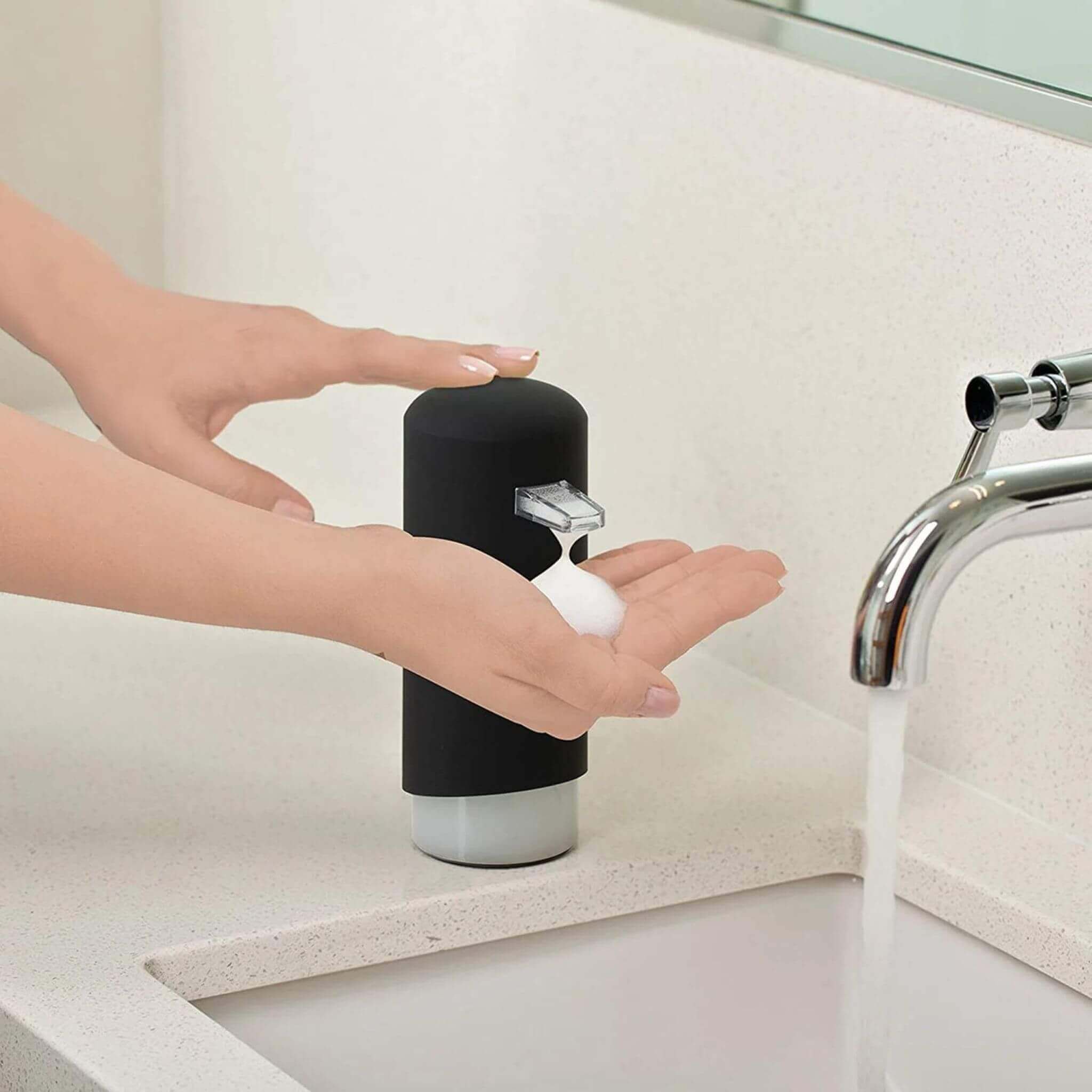 women using a black modern foam dispenser on a wash basin with water running out of the tap