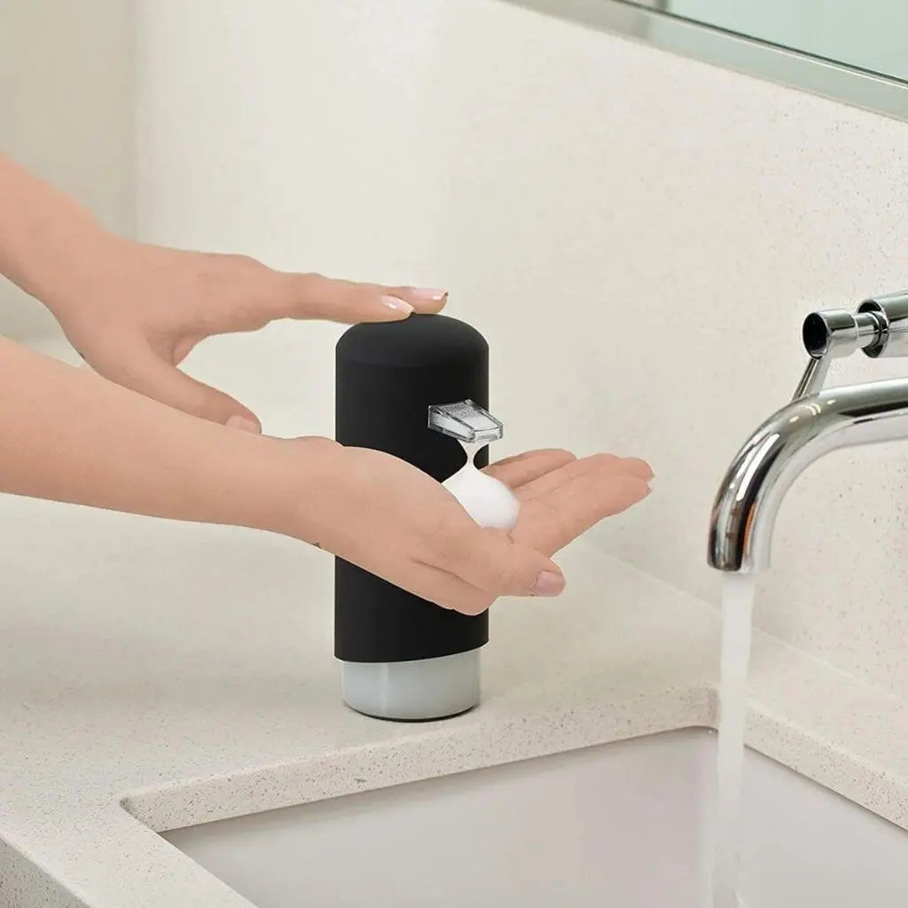 Person using a black soap dispenser on hands in a bathroom setting