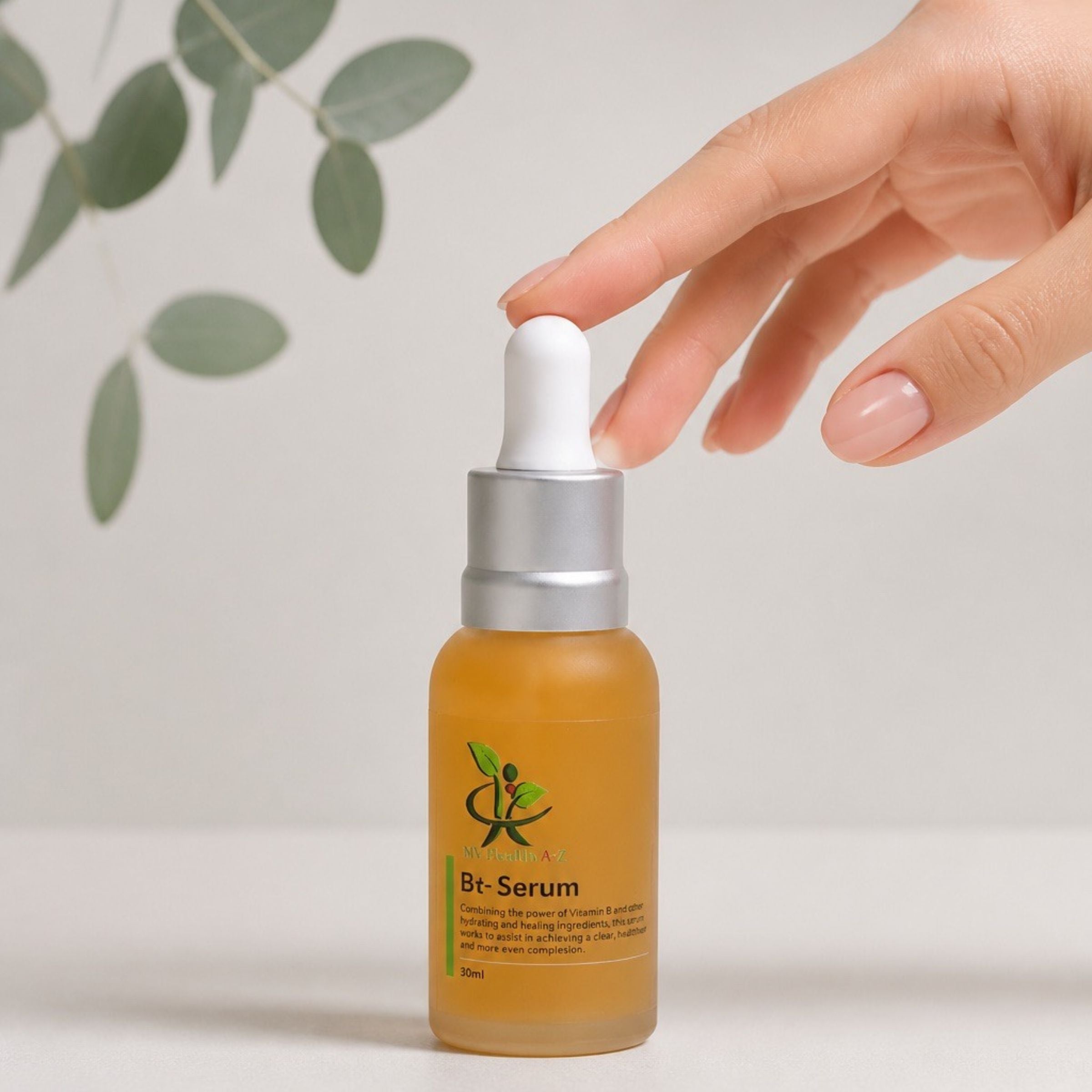 A hand with manicured nails is about to press the white dropper cap of a small amber glass bottle labelled &