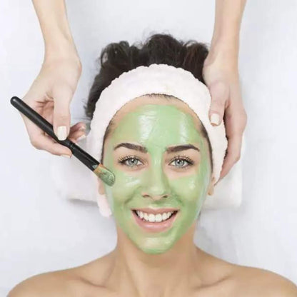 Woman applying green facial mask with a brush on a white background