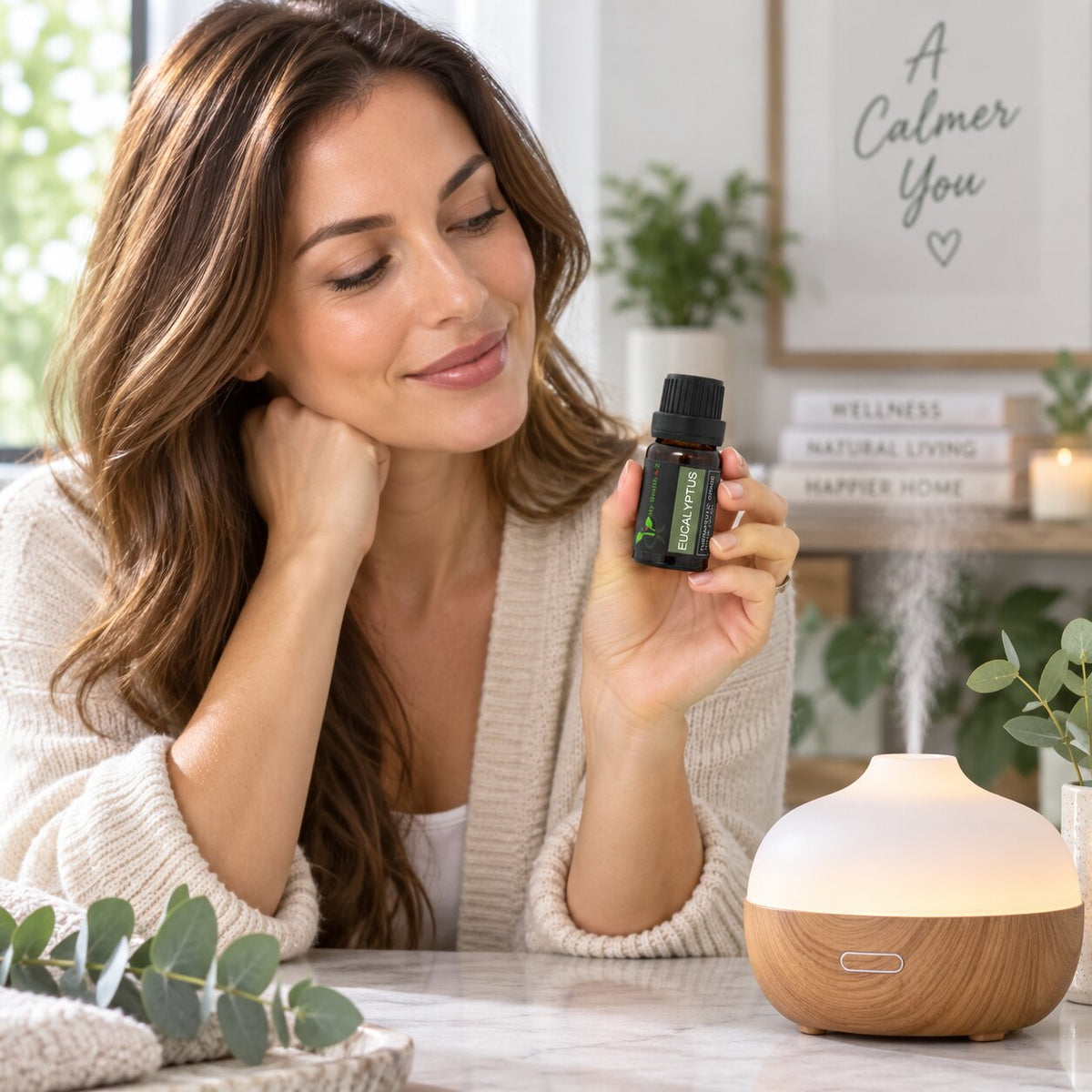 A woman holds a small essential oil bottle labelled Eucalyptus near a glowing diffuser on a table in a cozy, softly lit room.