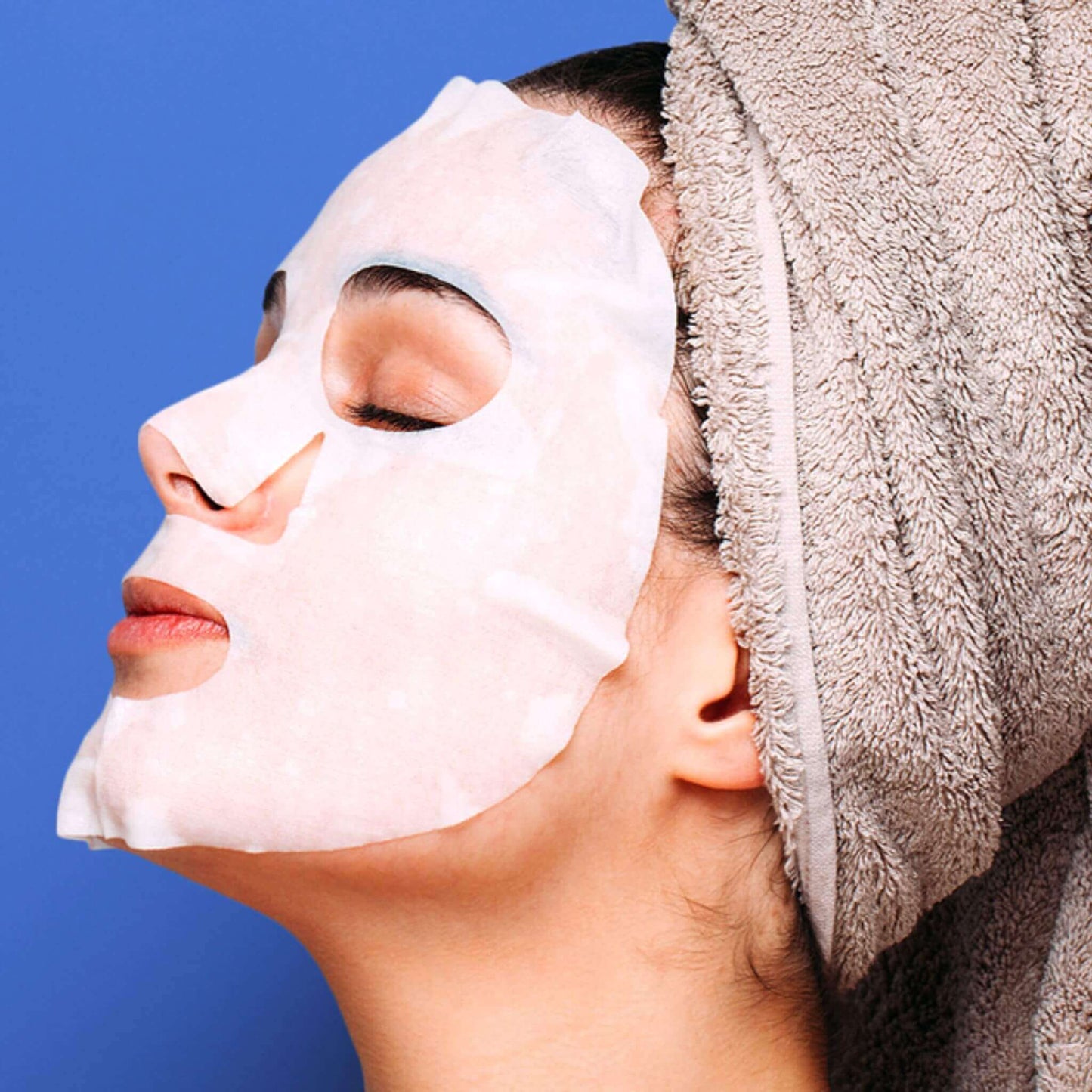 Person with a face 'My Health A-Z' exfoliating sheet mask and towel on a blue background