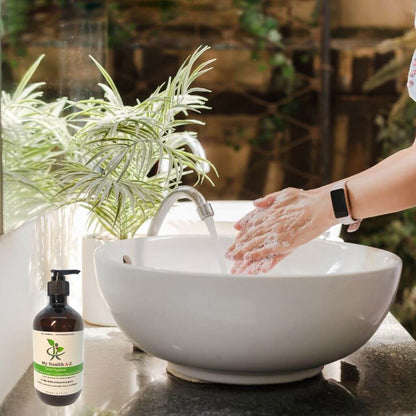 Person washing hands under a faucet with a bottle of soap next to a sink, surrounded by plants.