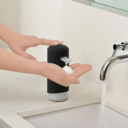 Person using a black soap dispenser on hands in a bathroom setting