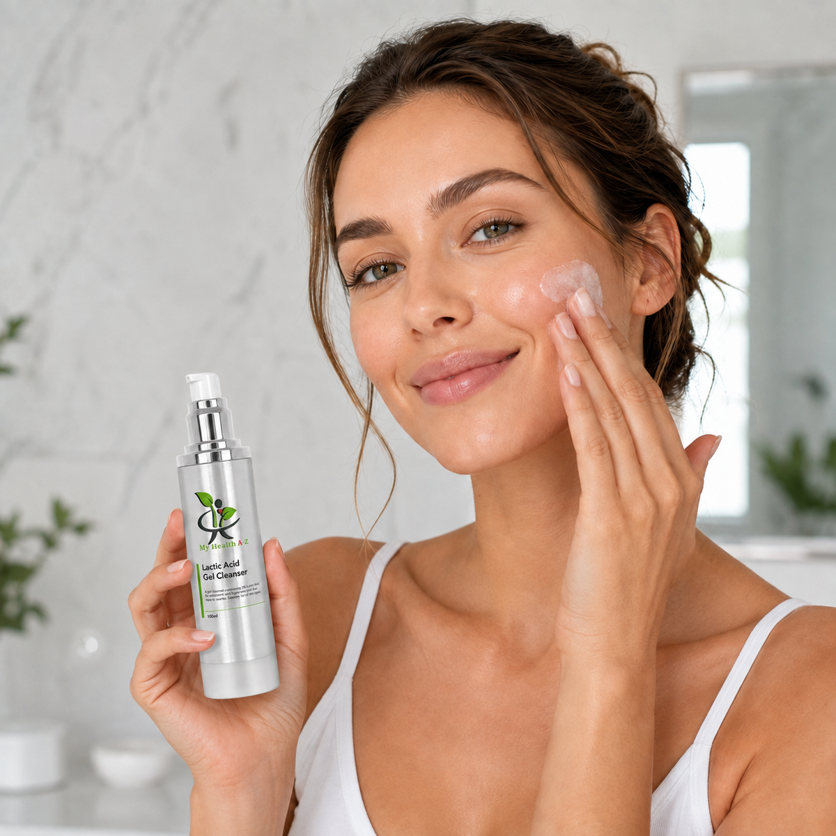 A woman with her hair in a bun applies cream to her face while holding a silver bottle applying face Lactic Acid Gel Cleanser to her face in a bright bathroom setting.
